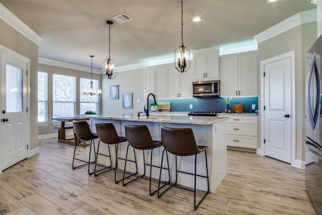 kitchen featuring visible vents, a notable chandelier, ornamental molding, stainless steel microwave, and tasteful backsplash