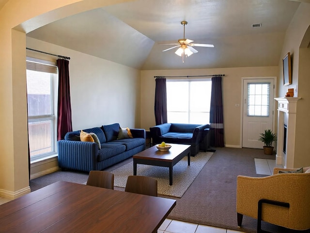 carpeted living room featuring a ceiling fan, visible vents, lofted ceiling, a fireplace with flush hearth, and arched walkways