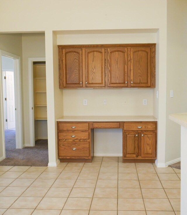 kitchen featuring brown cabinetry, light tile patterned floors, built in study area, and light countertops