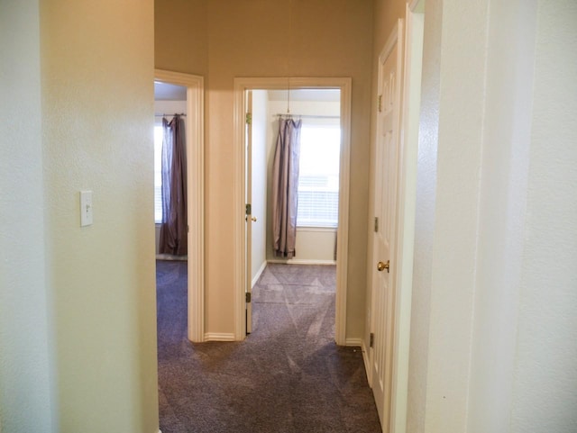 hallway featuring baseboards and dark colored carpet
