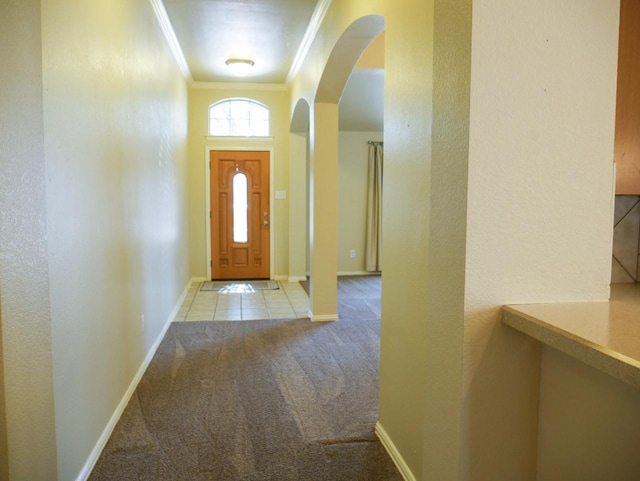 carpeted foyer entrance featuring tile patterned flooring, baseboards, ornamental molding, a textured wall, and arched walkways