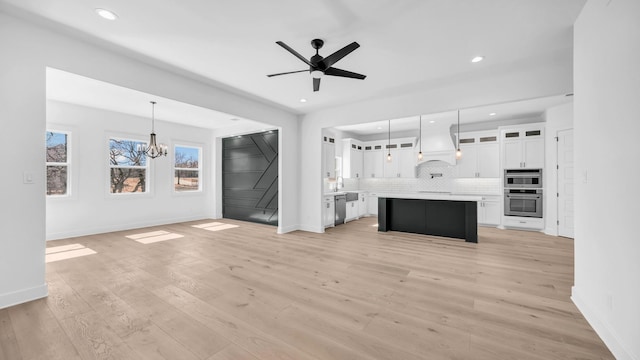 unfurnished living room with recessed lighting, ceiling fan with notable chandelier, light wood-type flooring, and baseboards