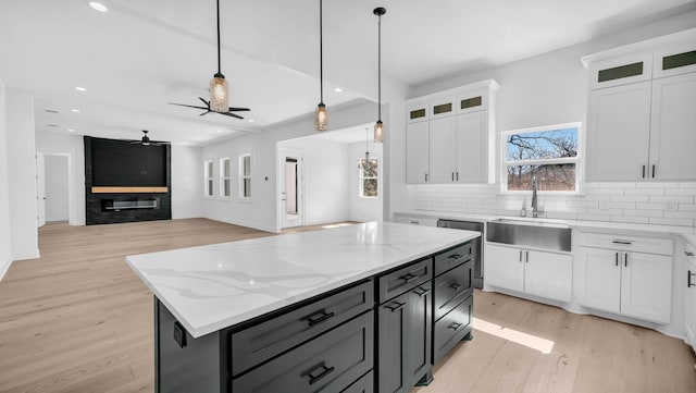 kitchen with a sink, white cabinets, light wood-style floors, tasteful backsplash, and a large fireplace