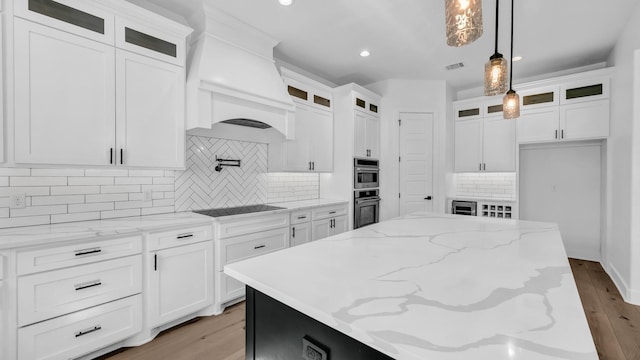 kitchen with light wood finished floors, a center island, decorative light fixtures, light stone counters, and white cabinetry