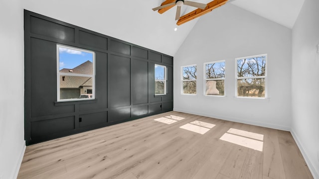 unfurnished bedroom featuring a decorative wall, light wood-style flooring, baseboards, and high vaulted ceiling