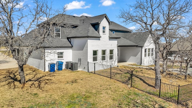 back of property with fence, a yard, a shingled roof, brick siding, and central AC unit