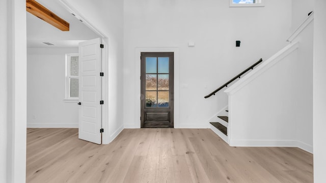 foyer entrance featuring visible vents, baseboards, light wood-style floors, and stairs