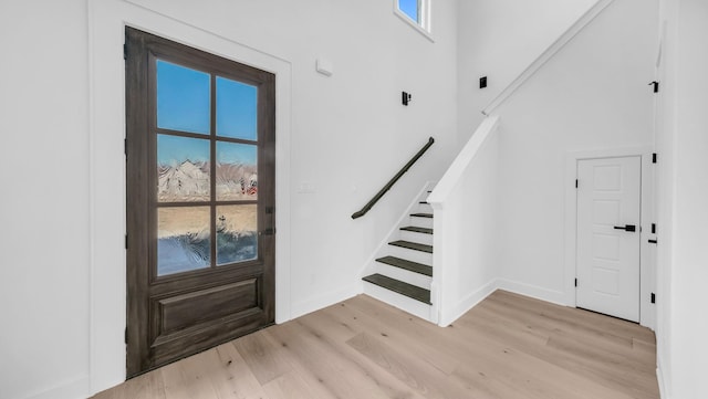 entryway featuring stairs, a towering ceiling, baseboards, and light wood finished floors