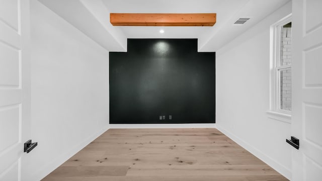 unfurnished room with beamed ceiling, light wood-style floors, visible vents, and baseboards