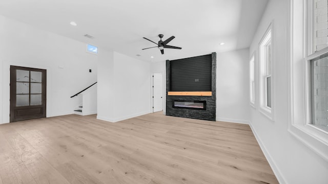 unfurnished living room with light wood-type flooring, visible vents, a fireplace, ceiling fan, and stairs