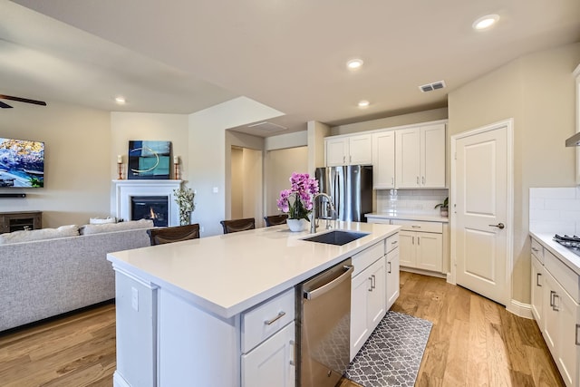 kitchen with visible vents, a warm lit fireplace, open floor plan, stainless steel appliances, and decorative backsplash