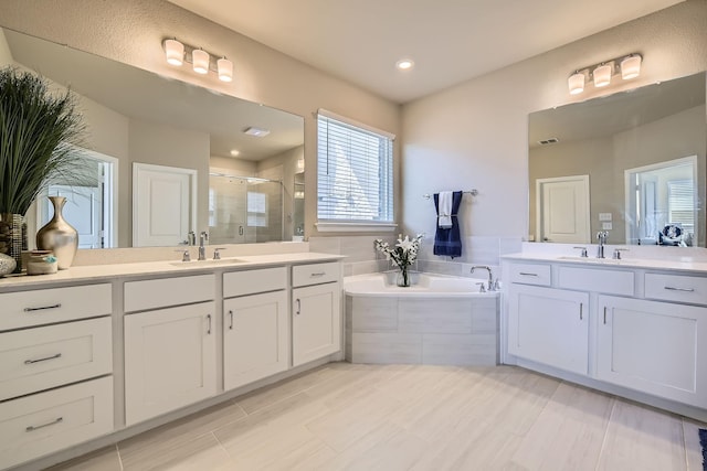 full bathroom with a shower stall, two vanities, a garden tub, and a sink