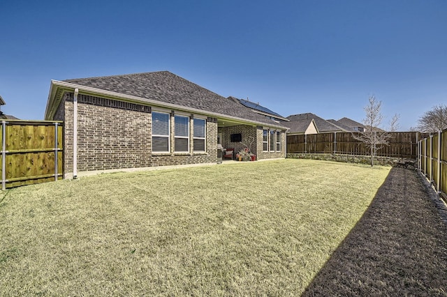 back of house with a yard, brick siding, and a fenced backyard