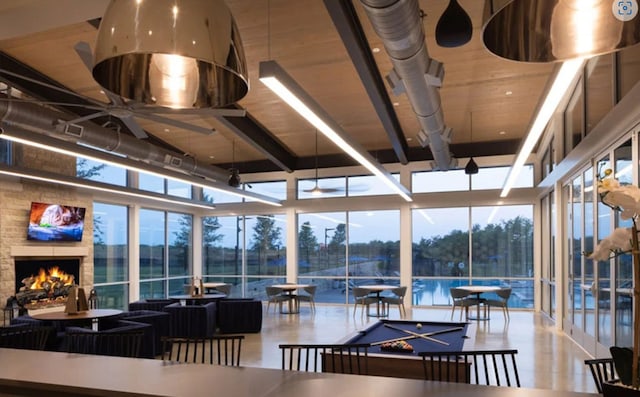 interior space featuring a ceiling fan, expansive windows, a healthy amount of sunlight, and a lit fireplace