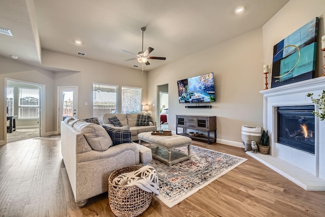 living room featuring visible vents, a glass covered fireplace, wood finished floors, recessed lighting, and baseboards