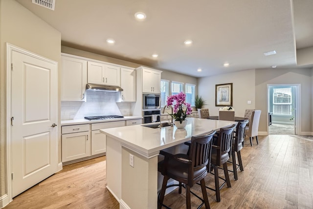 kitchen with visible vents, a kitchen island with sink, light wood-style floors, under cabinet range hood, and appliances with stainless steel finishes