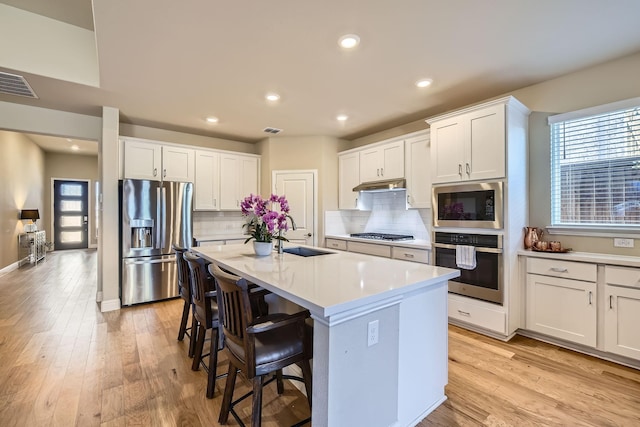 kitchen with a kitchen bar, visible vents, light wood-type flooring, under cabinet range hood, and stainless steel appliances