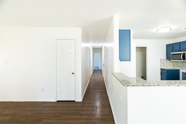 hallway with dark wood-style floors, a textured ceiling, and baseboards