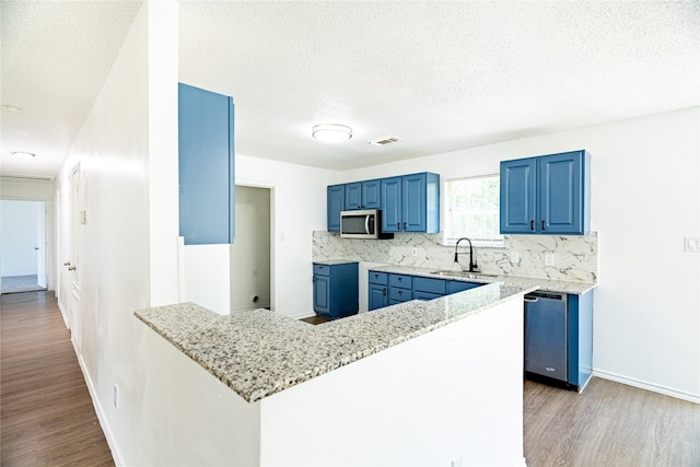 kitchen with a sink, blue cabinetry, tasteful backsplash, stainless steel appliances, and a peninsula