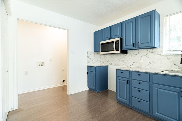 kitchen with stainless steel microwave, blue cabinets, dark wood-style floors, and backsplash