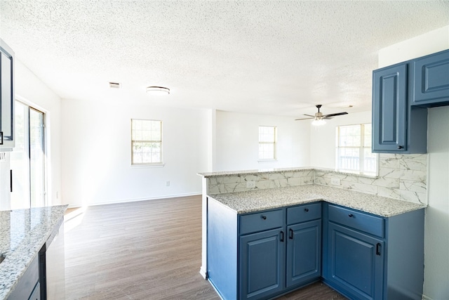 kitchen with dark wood finished floors, decorative backsplash, blue cabinetry, and a peninsula