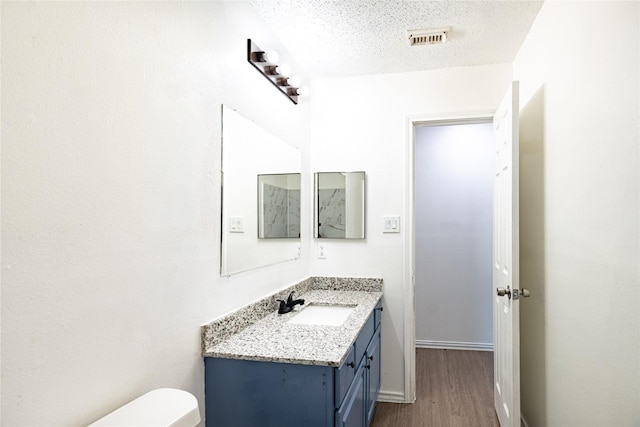 half bathroom with visible vents, toilet, vanity, wood finished floors, and a textured ceiling