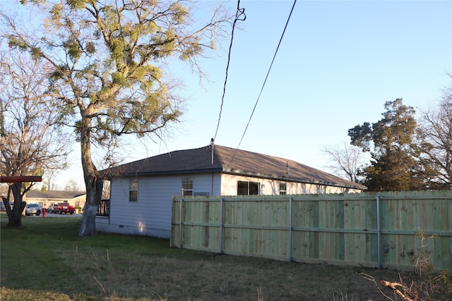 view of side of home featuring crawl space, a lawn, a shingled roof, and fence