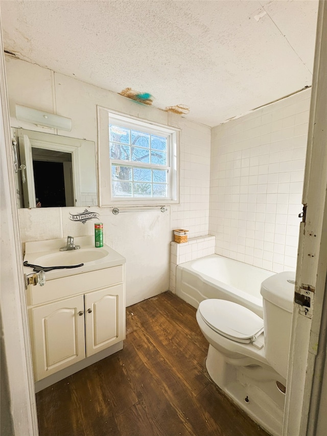 bathroom featuring toilet, vanity, a bathtub, wood finished floors, and a textured ceiling