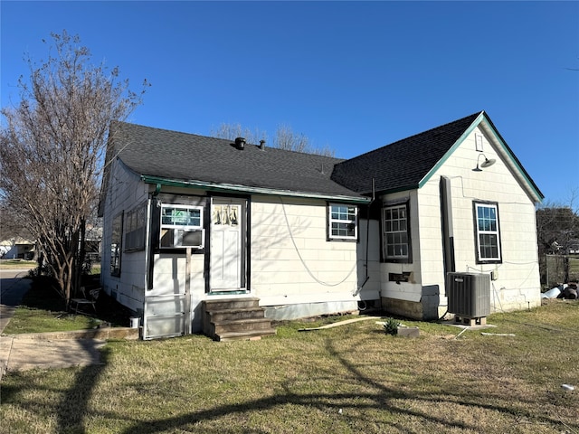 rear view of house featuring entry steps, a yard, central AC unit, and a shingled roof