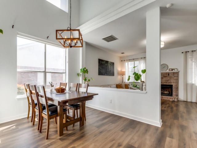 dining space with visible vents, dark wood-type flooring, an inviting chandelier, baseboards, and a brick fireplace