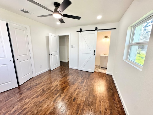 unfurnished bedroom with a barn door, wood finished floors, visible vents, baseboards, and ensuite bathroom