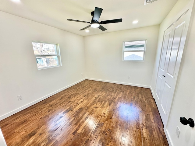 unfurnished bedroom with baseboards, dark wood-style flooring, multiple windows, and a closet