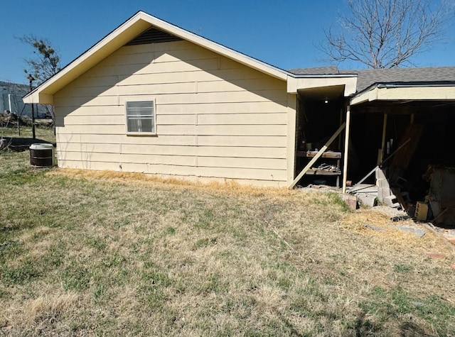 view of side of home with a yard, central AC unit, and roof with shingles