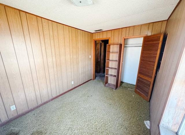 unfurnished bedroom featuring visible vents, wood walls, carpet floors, a closet, and a textured ceiling