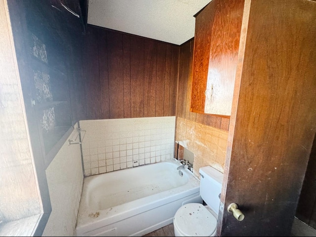 bathroom with toilet, a bath, wooden walls, and a textured ceiling