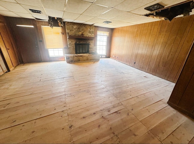 unfurnished living room featuring a drop ceiling, a fireplace, light wood-style floors, and wood walls