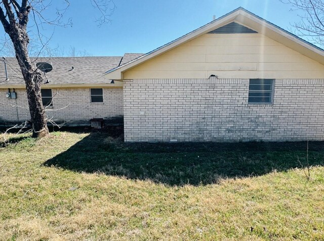 view of side of property featuring brick siding, a lawn, and a shingled roof