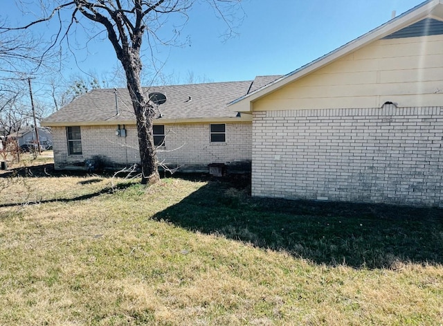 view of home's exterior with a yard, brick siding, and a shingled roof