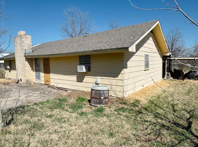 back of property featuring a patio area, a yard, a chimney, and roof with shingles