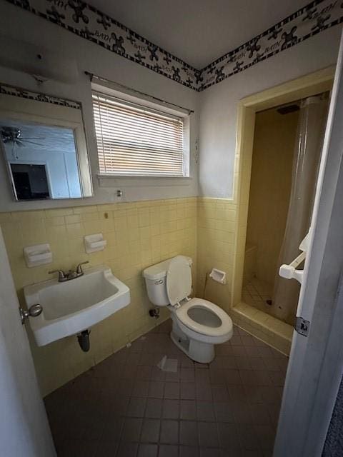 bathroom featuring a wainscoted wall, toilet, a stall shower, tile walls, and a sink