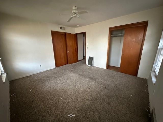 unfurnished bedroom featuring visible vents, ceiling fan, carpet, and multiple closets