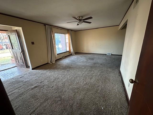 carpeted spare room with visible vents, baseboards, and a ceiling fan