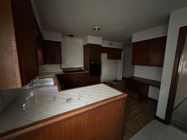 kitchen with tile counters, black oven, and a sink