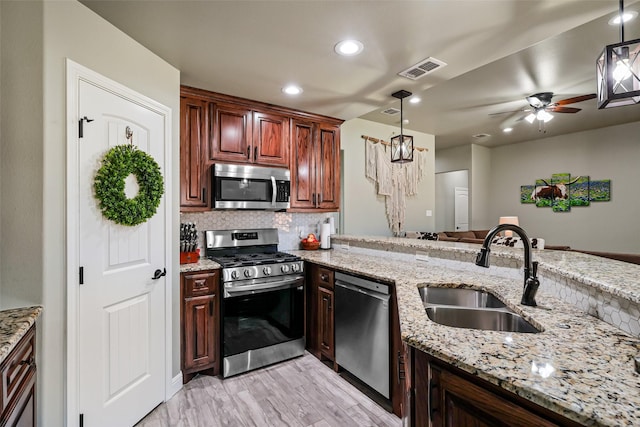 kitchen with light stone counters, a sink, decorative backsplash, appliances with stainless steel finishes, and pendant lighting