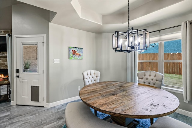 dining area with a tray ceiling, wood finished floors, baseboards, and a warm lit fireplace