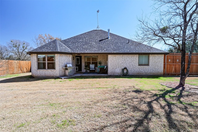 back of property with a yard, a fenced backyard, brick siding, and a shingled roof