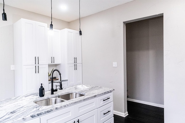 kitchen featuring white cabinets, light stone countertops, baseboards, and a sink