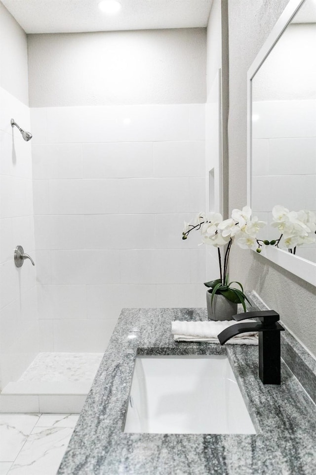 bathroom with marble finish floor, a tile shower, and a sink