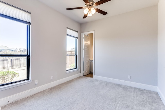 carpeted spare room featuring baseboards, a wealth of natural light, and ceiling fan