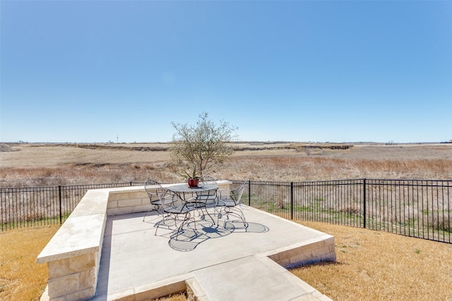 view of patio with a rural view, outdoor dining space, and fence